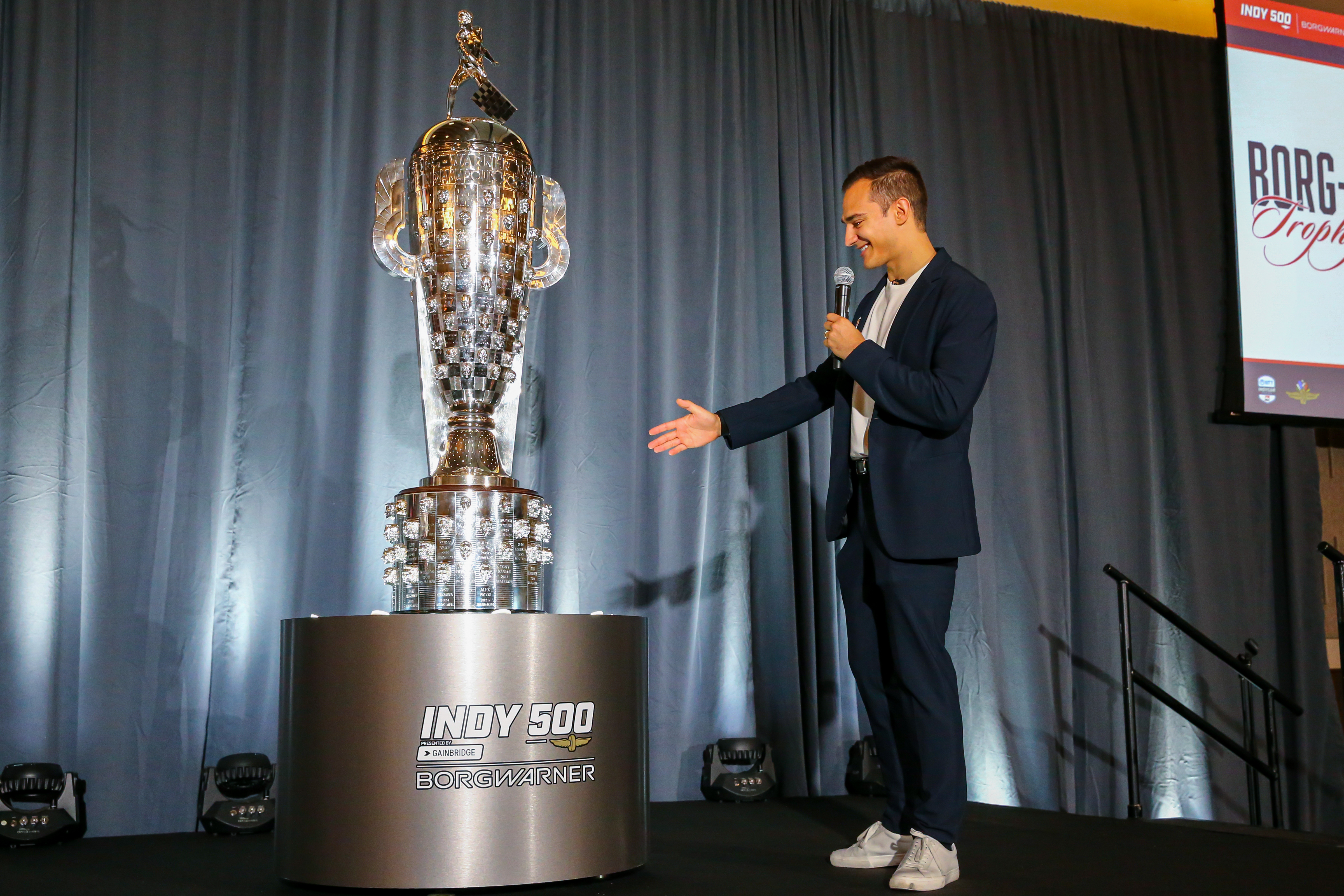 Man onstage points at silver trophy