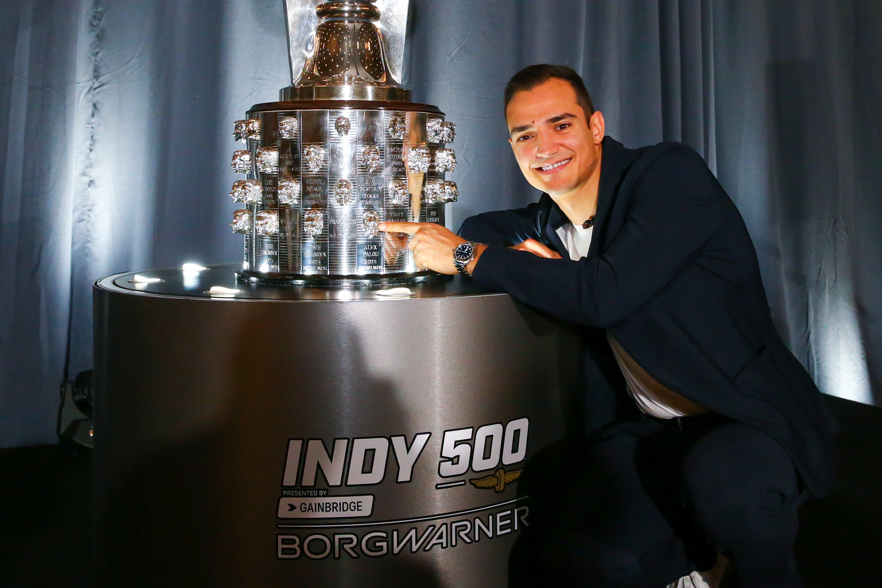 Man smiles and points at silver trophy
