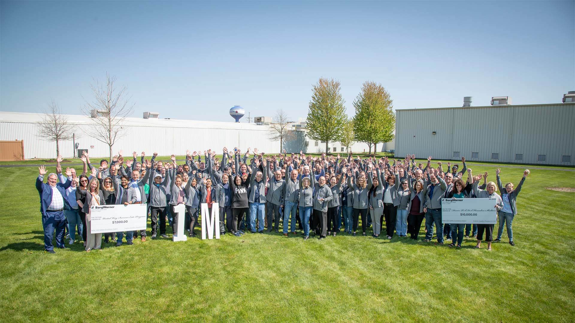 Large group of people cheer on green field with industrial buildings in the back