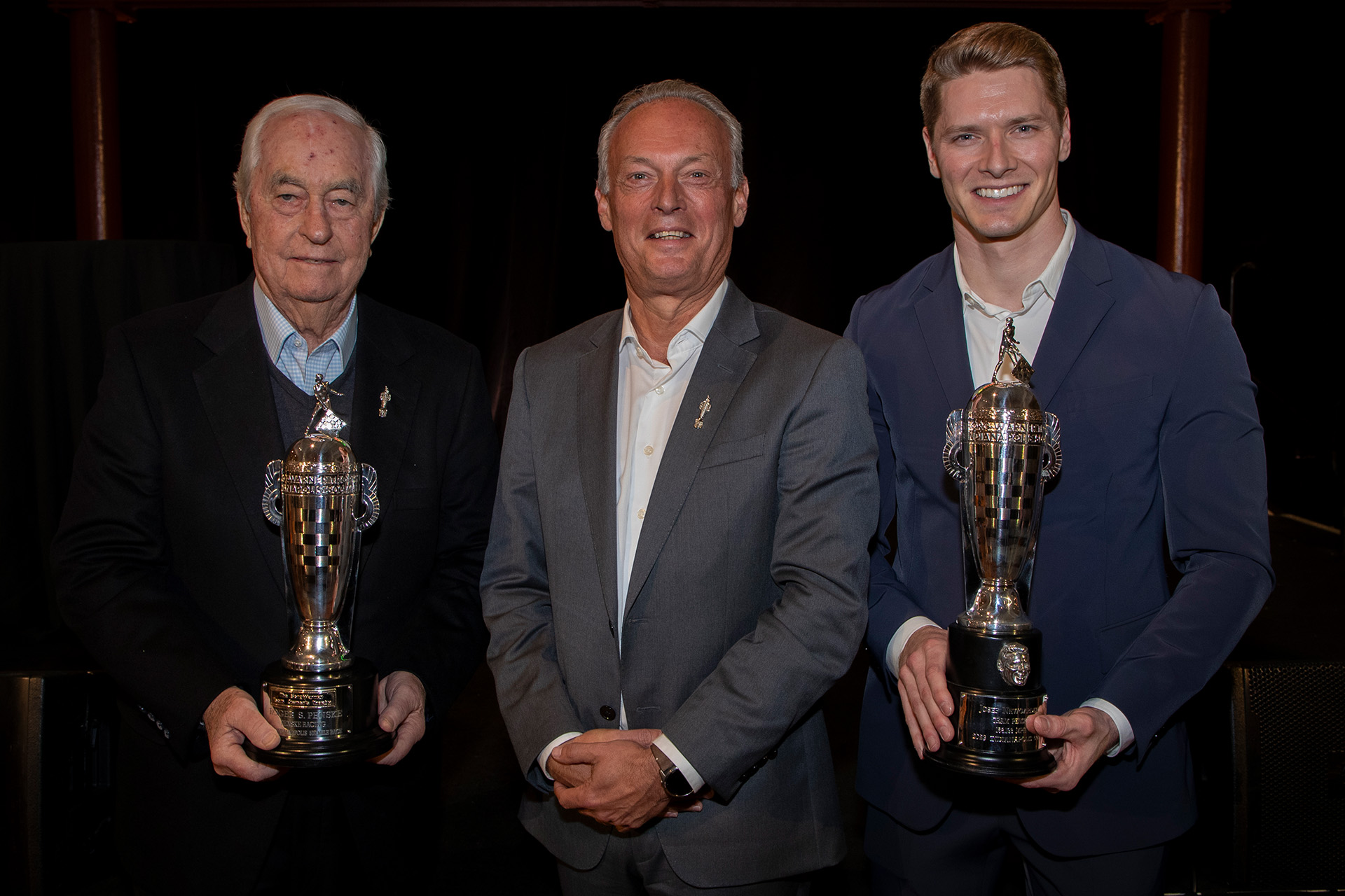 Three men stand and smile while two hold trophies