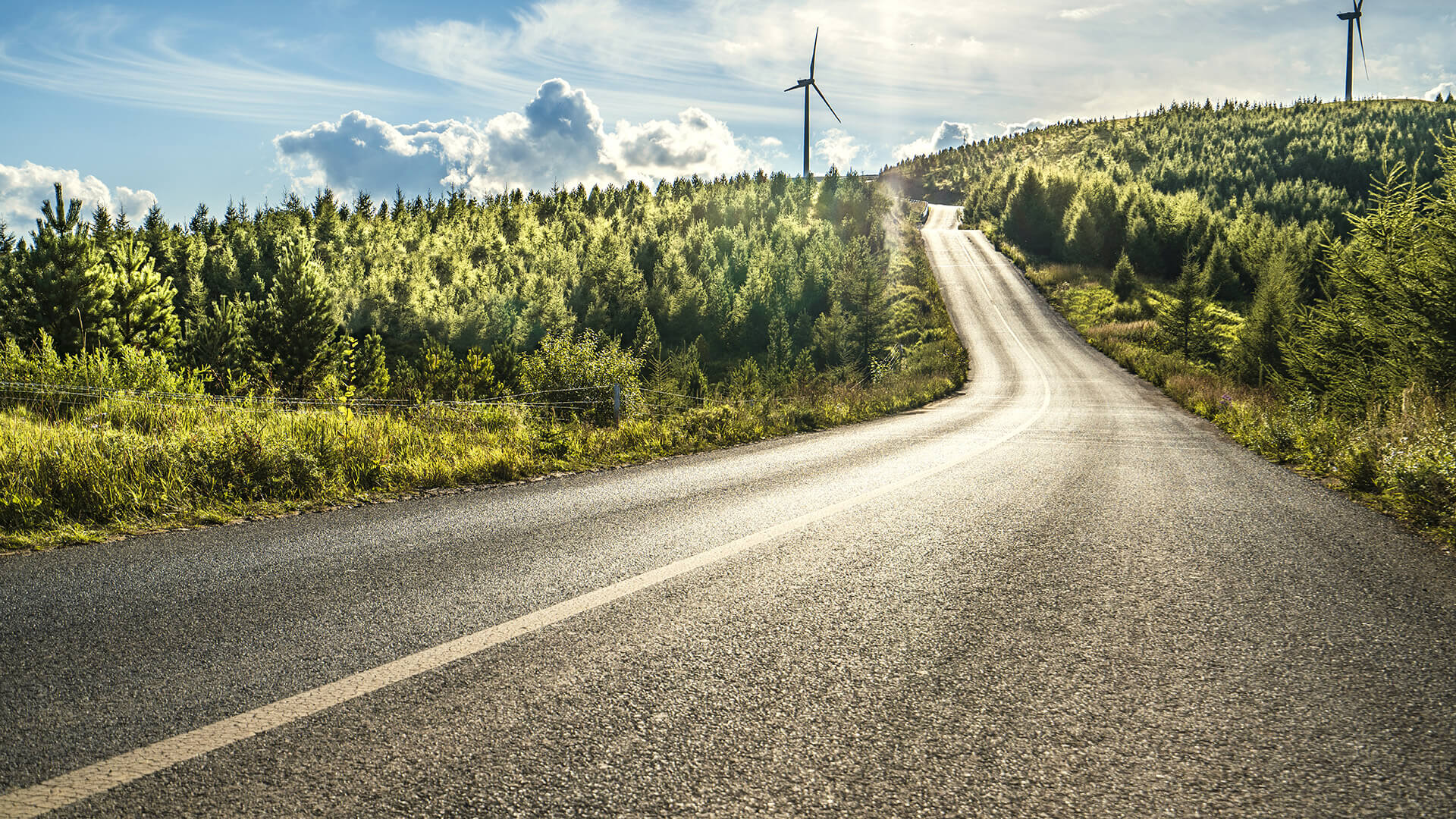 a road through countryside at sunset wind turbines in the background