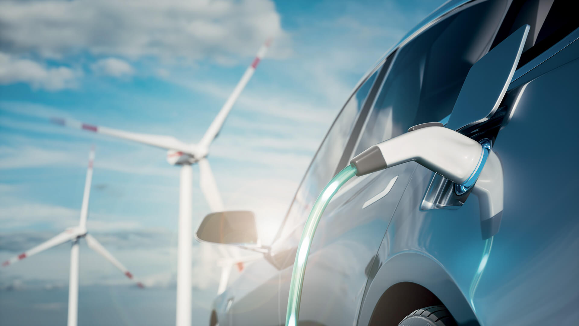 an electric car connected to a charging cable while a wind turbine is in the background