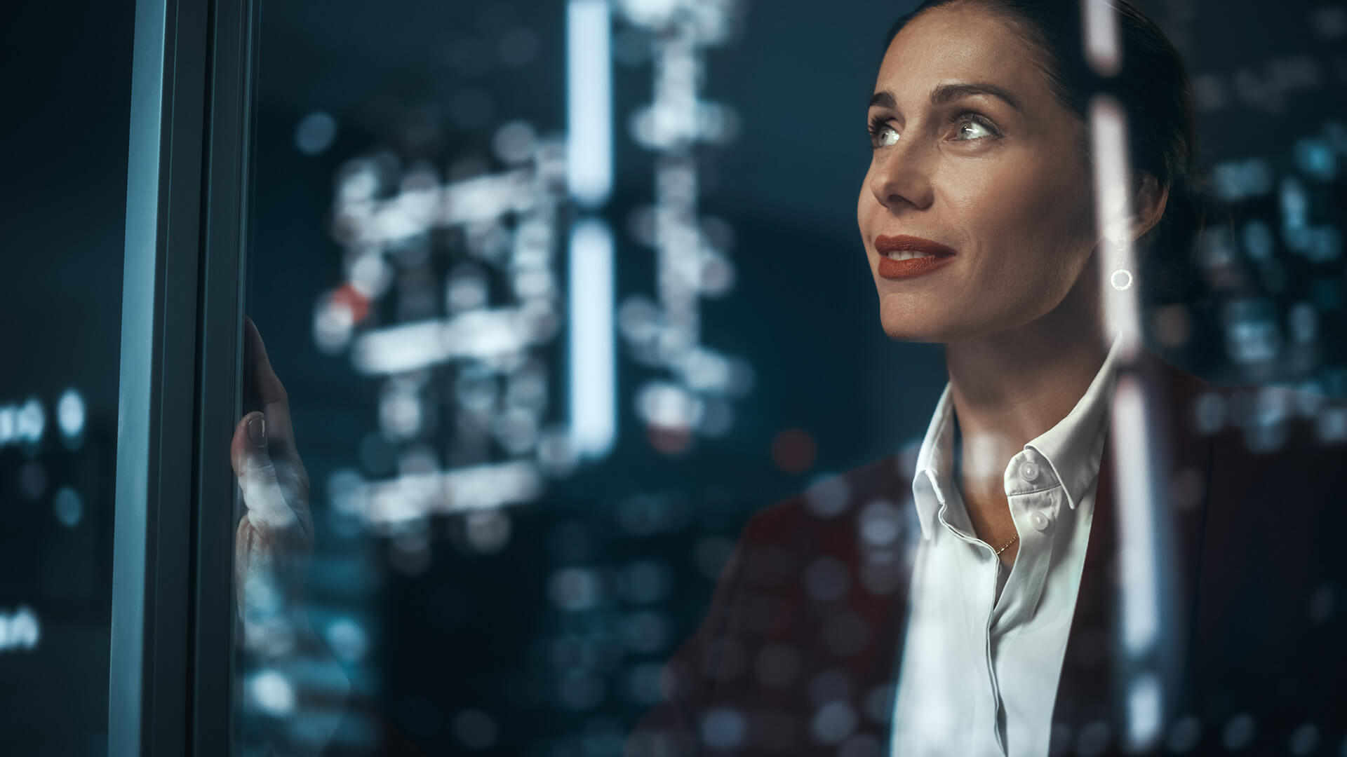a woman looking through an office building window in a city at night
