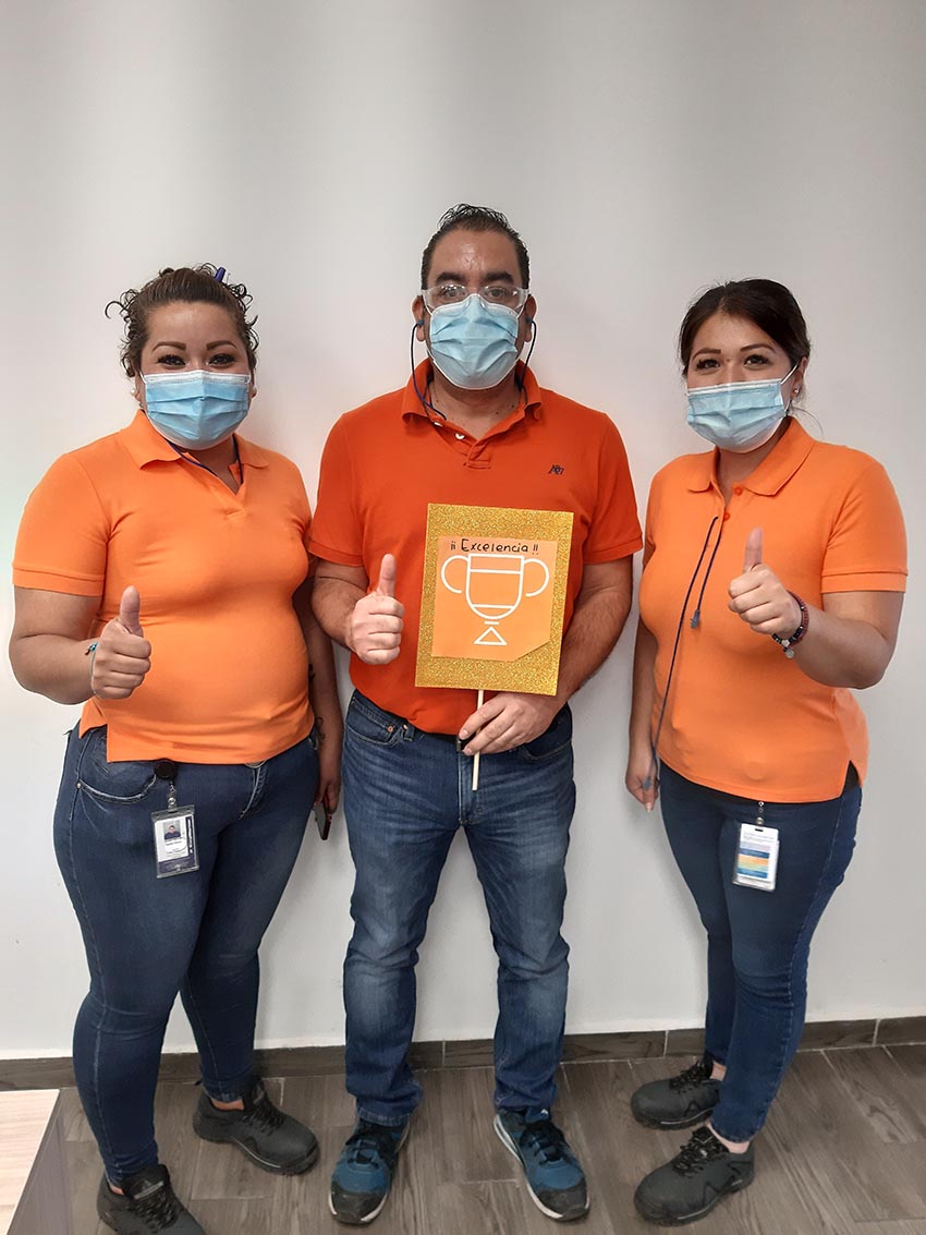 Three people in orange shirts holding a photo of a trophy